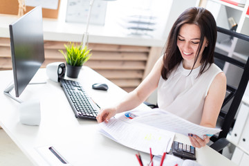 A young girl sitting in the office at a computer Desk and working with documents and a calculator.