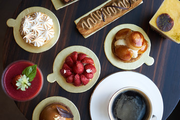 Breakfast time with cup of hot coffee and pieces of cream cake with strawberries and raspberries, sweets dessert breakfast snacks, close-up. Berry cupcakes dessert on wooden table background, top view