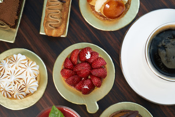 Breakfast time with cup of hot coffee and pieces of cream cake with strawberries and raspberries, sweets dessert breakfast snacks, close-up. Berry cupcakes dessert on wooden table background, top view