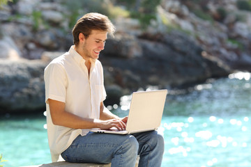 Happy guy uses a laptop on summer vacation