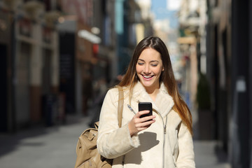 Happy lady using a smart phone in winter on the street