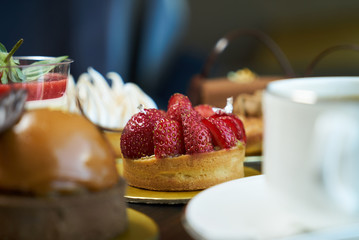 Breakfast time with cup of hot coffee and pieces of cream cake with strawberries and raspberries, sweets dessert breakfast snacks, close-up. Berry cupcakes dessert on wooden table background
