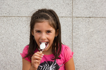 Little girl laughing while eating chocolate icecream. Smiling young kid portrait on pink t shirt...