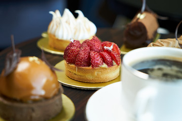 Breakfast time with cup of hot coffee and pieces of cream cake with strawberries and raspberries, sweets dessert breakfast snacks, close-up. Berry cupcakes dessert on wooden table background
