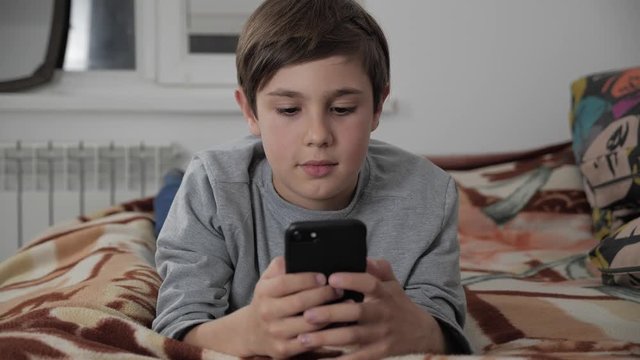 Child Boy Playing with Mobile Phone at Home. Kid Using Smartphone lying on a bed
