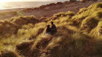 Aerial view over a young couple sitting on the beach at sunset