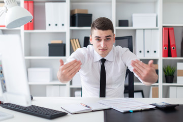 A young man sitting at a computer Desk in the office and spread his hands to the side.