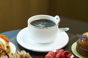Morning breakfast time with cup of hot coffee and pieces of cream cake with strawberries and raspberries, sweets dessert breakfast snacks, close-up. Berry cupcakes dessert on table background