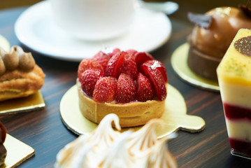 Morning breakfast time with cup of hot coffee and pieces of cream cake with strawberries and raspberries, sweets dessert breakfast snacks, close-up. Berry cupcakes dessert on table background
