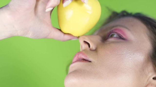 Beautiful woman looking at fresh yellow apple, posing into camera, close-up