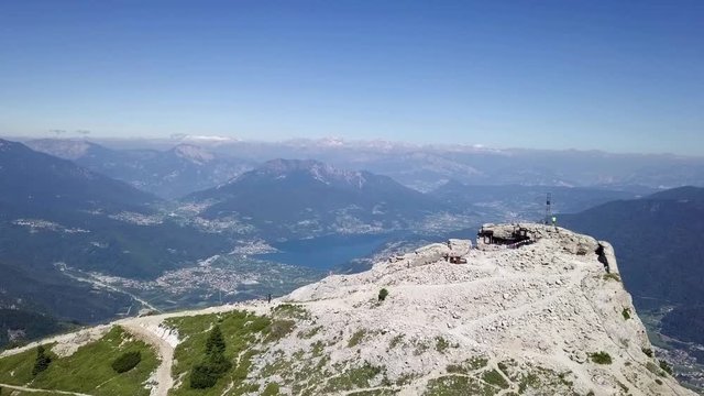 Aerial view of a young man standing in top of Cima Vezzena, Pizzo di Levico, with drone flying forward with panoramic views of Trento, Italy