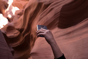 HAND OF A WOMAN HOLDING SMART PHONE TRYING TO TAKE A BEAUTIFUL PHOTO OF ANTELOPE CANYON , ARIZONA , USA