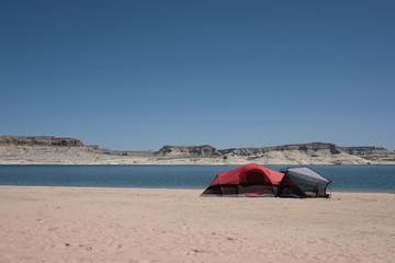 A RED TENT ON BEACH WITH BACKGROUND OF BEAUTIFUL BLUE SEA AND ROCK MOUNTAIN / BEACH CAMPING ON LAKE POWELL , UTAH , ARIZONA , USA