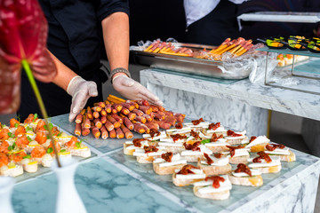 Waiter's hands in black gloves spread on the banquet table, where there are already other canapes