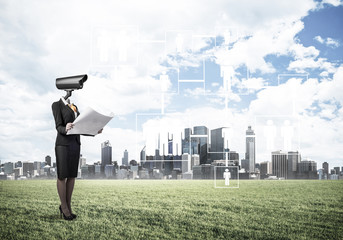 Camera headed woman standing on green grass against modern citys