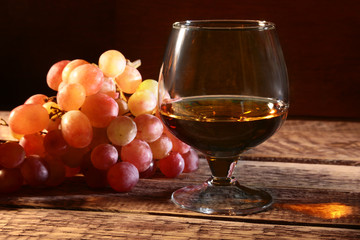 Cognac or Brandy in a glass and fresh grapes, still life in rustic style, vintage wooden background, selective focus.
