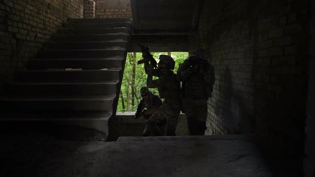 Elite squad of special force marines fully equppied and armed storming building captured by enemy during anti terrorism operation. Army soldiers climbing up stairway and securing area during combat.