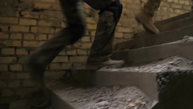 Closeup of special forces marines legs in old army boots climbing up dusty staircase in ruined building captured by enemy during military operation. Elite squad of army soldiers storming the building.