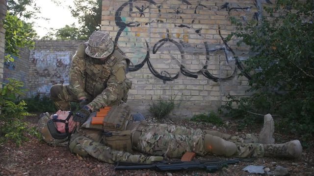 Heroic army ranger medic in uniform saving life of wounded brother in arms, dragging him away to safe place during combat. Army paramedic evacuating injured and unconscious comrade from battlefield.