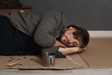 Obraz premium Poor homeless man sleeping on floor near dark wall