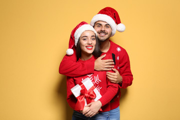 Young couple in Christmas sweaters and hats with gift on color background