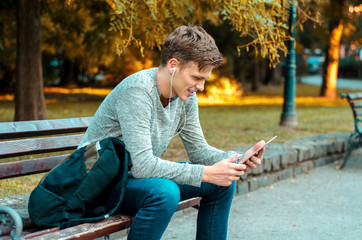 Obraz premium Teenager sitting on park bench after school and using tablet 