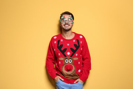 Young man in Christmas sweater with party glasses on color background