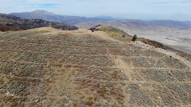 Aerial-Climbing sagebrush hill with three UTV off road vehicles parked on top, viewing erosion-control terracing done by the CCC in the 1930's to reveal fall colors in the valley beyond.