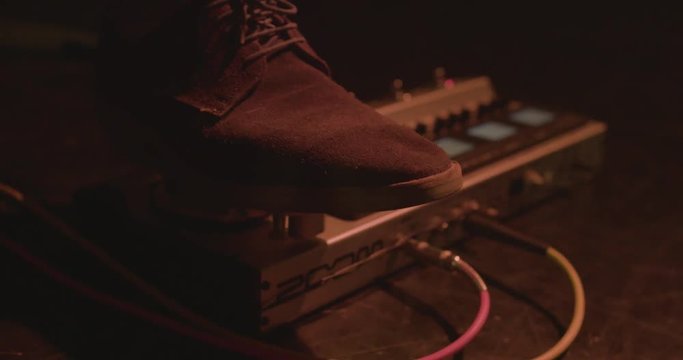 Foot in gumshoes pressing on loop pedal for electric guitar. Close up of guitarist step on effect machine on concert scene.