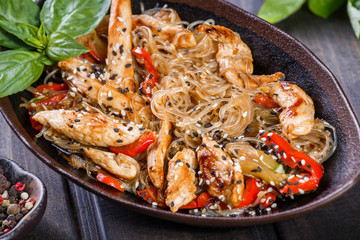 Rice noodles with chicken meat, vegetables and sesame seeds on wooden table. Indian cuisine. Top view