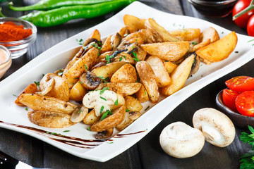 Roasted or baked potato with mushrooms, herbs, tomatoes and sauce on white plate on dark wooden background. Italian dish