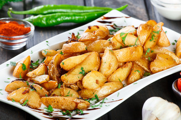 Roasted or baked potato with herbs, garlic, tomatoes and sauce on white plate on dark wooden background