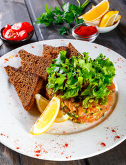 Tartar with salmon and avocado decorated with greens on plate on wooden table. Delicious appetizers