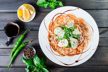 Fish carpaccio with arugula, crackers and cheese parmesan on dark wooden background. Delicious appetizers