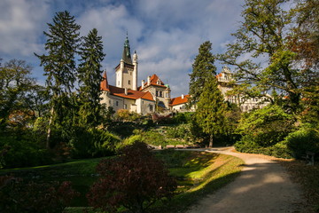 Fototapeta premium Scenic landscape of famous romantic Pruhonice castle, Czech Republic, Europe, standing on hill in a park, sunny fall day, blue sky, colorful trees, foot path with shadows of trees