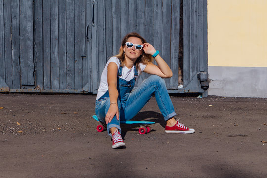 Portrait of a smiling woman sitting on her skateboard next to the old wooden wall.