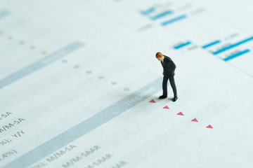 Miniature businessman looking at red down arrows of investment report, stock price drop, negative...