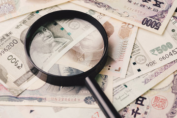 Magnifying glass on pile of asian leading countries new emerging market money banknotes, Indian rupee, Chinese yuan and Japanese yen, analyze, invest or searching for yield or financial concept