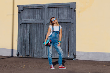 Portrait of a smiling woman standing with her skateboard next to the old wooden wall.