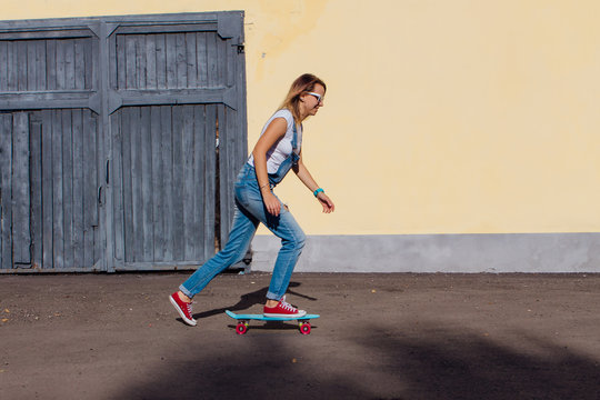 Portrait of a smiling woman riding on her plastic skateboard next to the old wooden wall.
