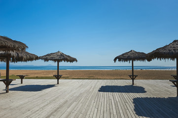 Empty beach, straw umbrellas on wooden flooring, bright sunny day, no season