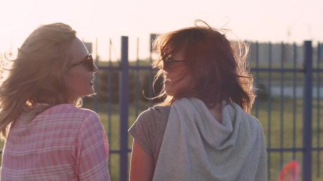 Two attractive girlfriends talking and laughing on treet. Sisters have a good time together. Slow motion 