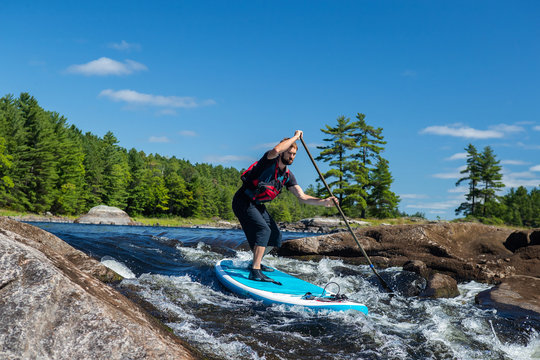 Man Paddling Whitewater On A A Stand Up Paddle Board