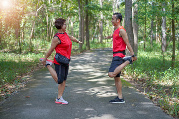 Fototapeta premium Happy senior asian woman with man or personal trainer stretch thigh muscles at park. Athletic senior exercising together outdoor. Elderly care exercise sport activity concept