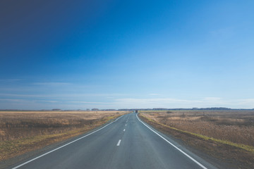 Empty road through the autumn fields. Toned image.