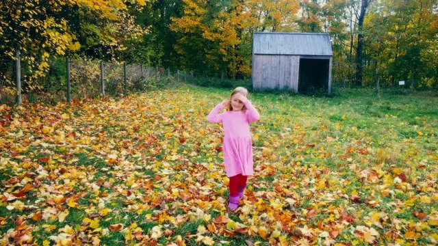 A young girl runs towards the camera throwing autumn leaves in fun, filmed in UHD 4K