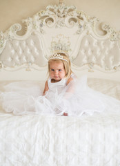 Fototapeta na wymiar So good to be the queen. Little child with long blond hair. Little girl wear tiara crown and hairstyle. Hair accessory. Small blond child sit on bed. Beautiful hairstyles for baby girls. Cute sweetie