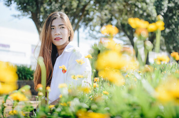 Portrait of beautiful young Asian woman sitting in the garden with yellow flowers foreground.