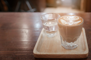 Close up glass cup of coffee on wooden table with sunlight in a cafe.