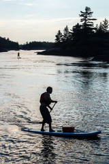 Silhouette of a man paddling on a a stand up paddle board in the Canadian wilderness